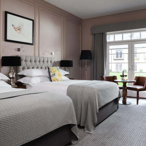 Elegant hotel room with twin beds, floral pillows, and a view of a garden.