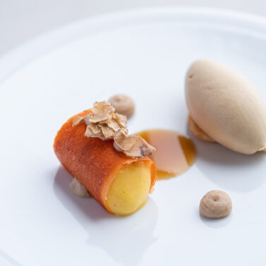 Exquisite dessert with orange fruit roll, ice cream scoop, and almonds on a white plate.