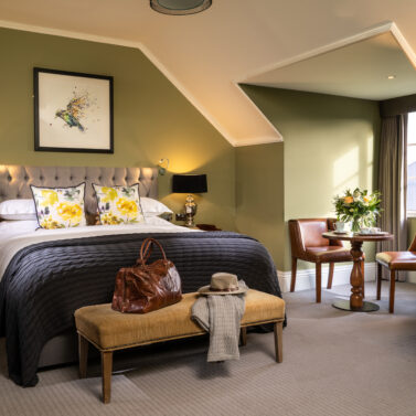 Elegant hotel room with a plush bed, cosy seating area by the window, inviting and warm ambience.