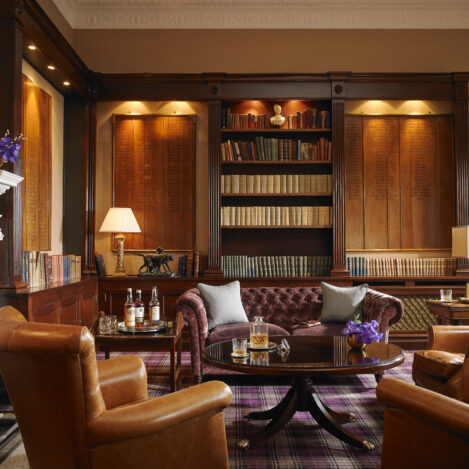 Cosy lounge with leather chairs, bookshelf, and fireplace, perfect for relaxing and socialising.