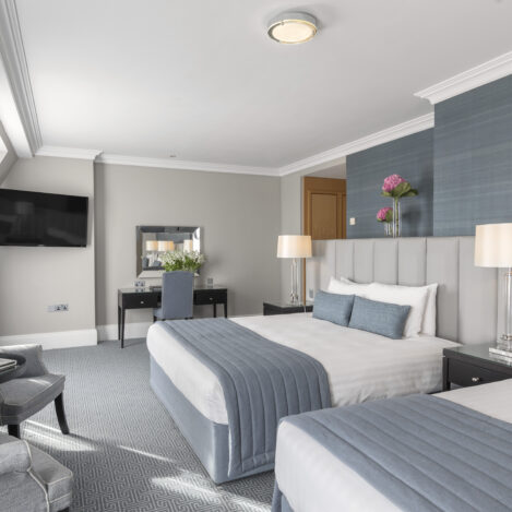 Elegant hotel room with two double beds, plush blue accents, and a cosy seating area.