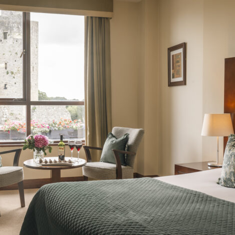 Cosy hotel room with a view of a historic tower, flowers, wine, and a seating area for two.