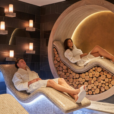 A couple relaxes in a cosy spa lounge with soft lighting and elegant décor.