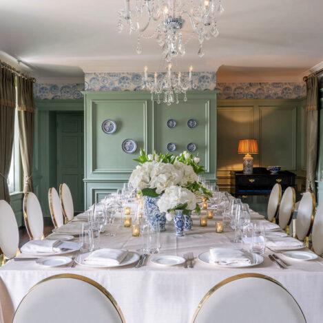 Elegant dining room with large table set for guests, featuring flowers and soft lighting.
