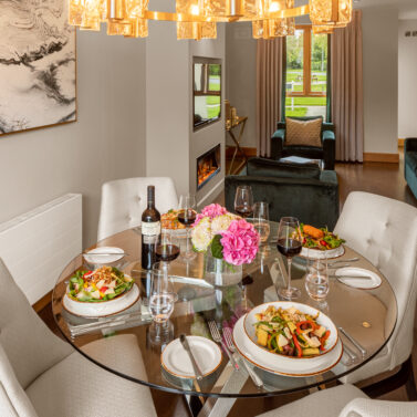 Cosy dining area with elegant decor, a glass table set for four with salads and wine.