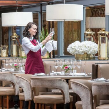 Waitress prepares elegant dining table with fresh flowers in upscale hotel restaurant.