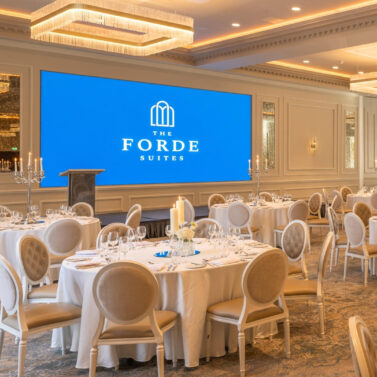 Elegant banquet hall set with round tables, fine dining settings, and a large screen.