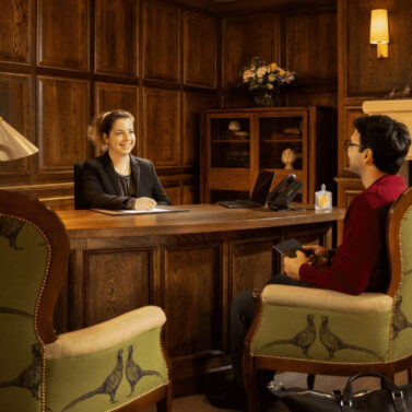 Welcoming hotel reception with smiling staff and a guest in a cosy, wood-panelled setting.