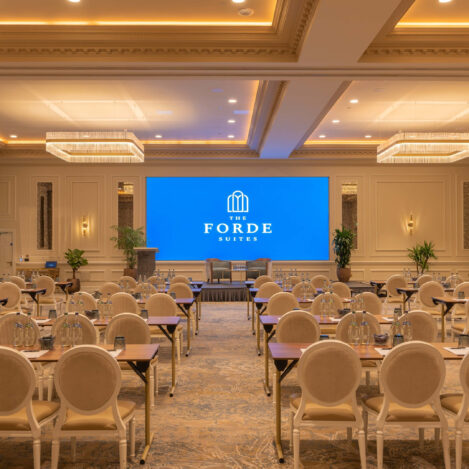 Elegant conference room setup with beige chairs, tables, and a large screen displaying "The Forde Suites".