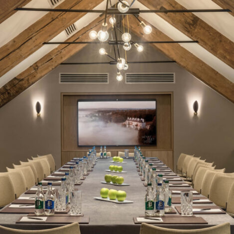 Elegant meeting room with a long table, green apples, water bottles, under warm lighting.