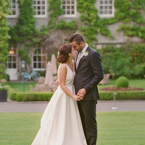 A couple embraces lovingly in a lush garden outside a charming, ivy-covered building.