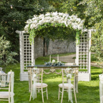 Elegant garden wedding venue with floral arch and decorated chairs.