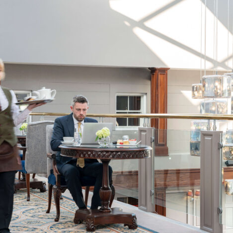 Businessman enjoying tea in a cosy hotel lounge as a waitress serves nearby. Elegant lighting.