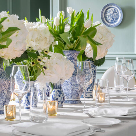 Elegant dining table with blue vases, white flowers, and candle holders in a cosy setting.