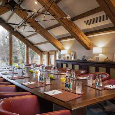 Cosy, well-lit meeting room with leather chairs, wooden beams, and scenic outdoor view.