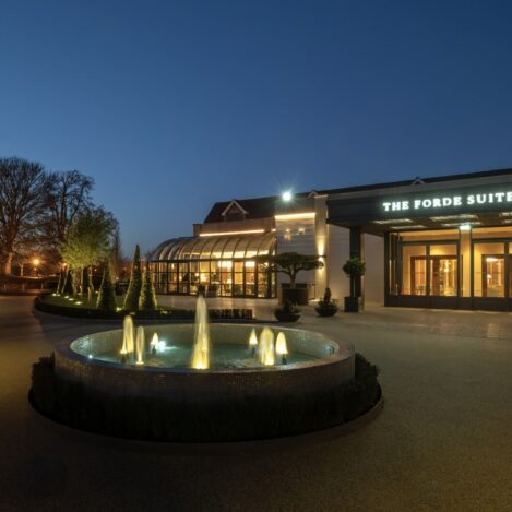 Evening view of The Forde Suites entrance with lit pathway and fountain.