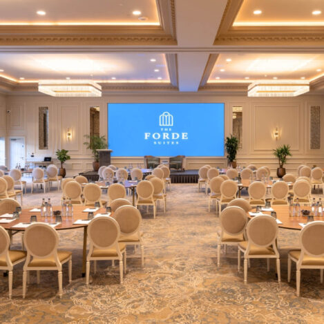 Elegant conference room with round tables, soft lighting and a large presentation screen.