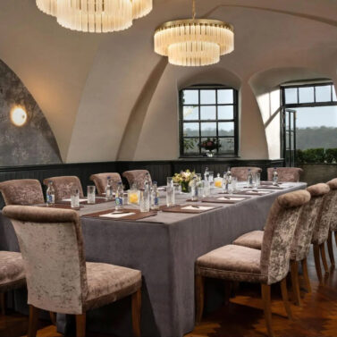 Elegant dining room in a hotel with classic decor, set for a gathering with plush chairs and a view outside.