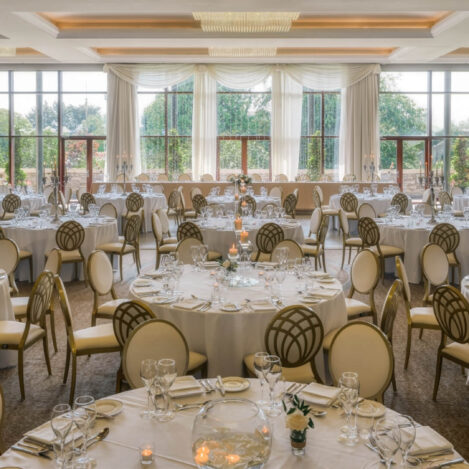 Elegant banquet hall set for a family gathering, with round tables, white linens, and large windows.