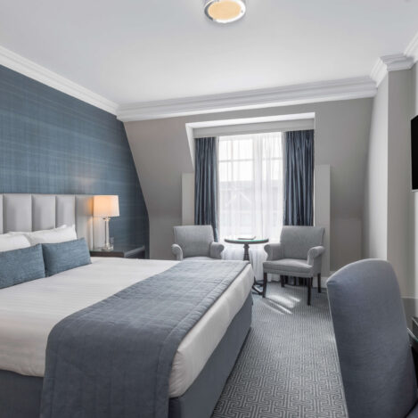 Inviting hotel room with a king bed, soft grey and blue decor, and a sitting area by a window.