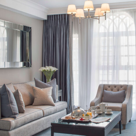 Elegant hotel room with cosy sofa, armchair, and coffee table set for tea, softly lit.