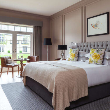 Elegant hotel room with plush bed, floral pillows, and large window view.