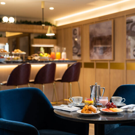 Elegant hotel dining area with a set breakfast table, featuring fruit, pastries, and hot drinks.
