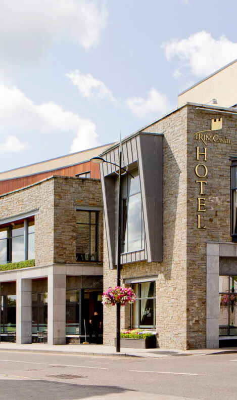 Elegant hotel exterior with stone facade under a clear sky, inviting entrance and vibrant flowers.