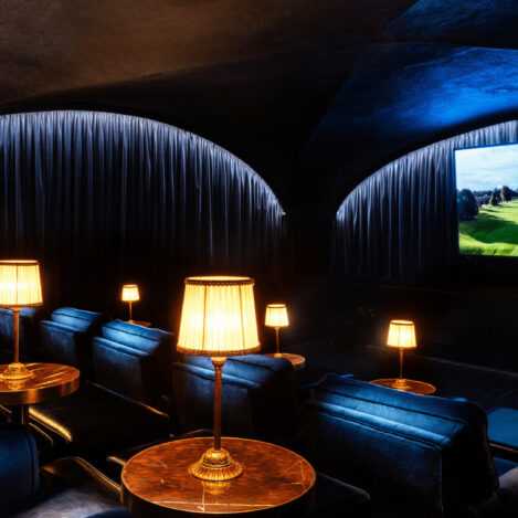 Cosy private cinema room with plush seating, warm lamps, and a large screen displaying a serene landscape.