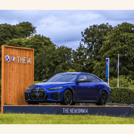 A sleek blue BMW i4 car displayed outdoors with lush greenery, showcasing elegance and innovation.