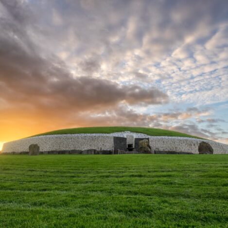 Ancient stone mound at sunrise with rolling green grass and dramatic sky.