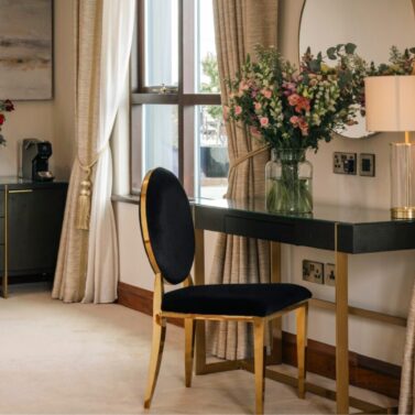 Elegant hotel room with plush seating, large windows, and floral decor creating a warm ambience.