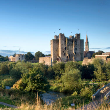 Majestic castle by a peaceful river surrounded by lush greenery at sunset.