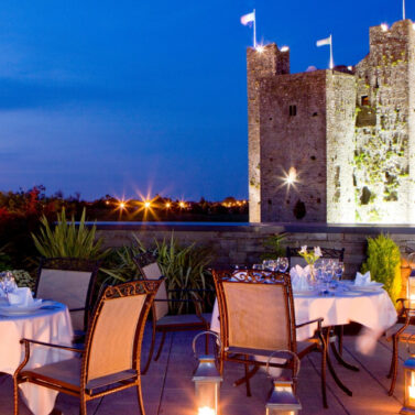 Romantic dinner setting overlooking a beautifully lit ancient castle at dusk.