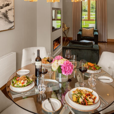 Elegant dining area in a cosy hotel suite with a set table, comfortable seating, and garden views.