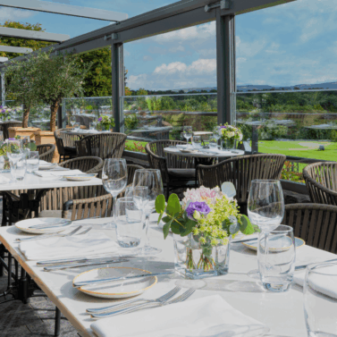 Scenic outdoor restaurant terrace with elegant table settings and a view of green countryside.