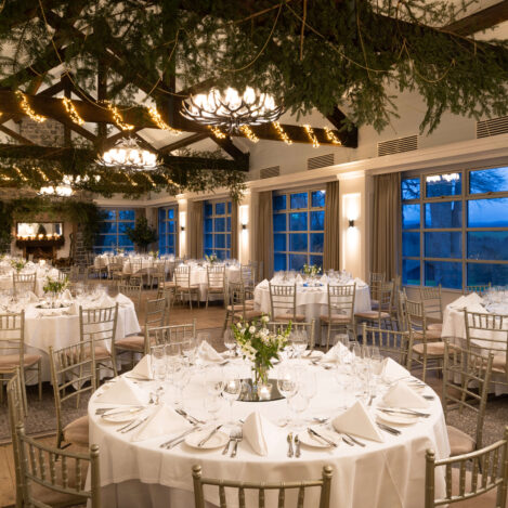 Elegant dining room with round tables set for an evening event, soft lighting and greenery.