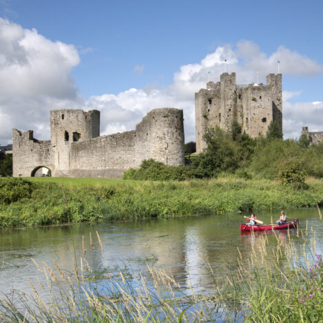 A couple canoeing on a river near an ancient castle under a bright blue sky.