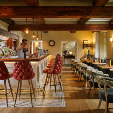 Cosy bar with armchairs and a bartender preparing drinks, warm lighting and inviting decor.